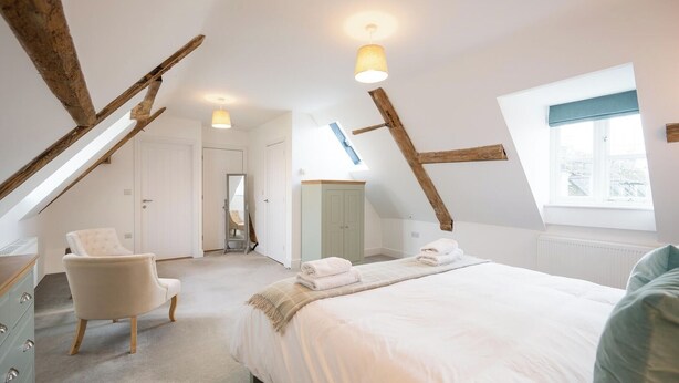 Une chambre avec un plafond en pente, un lit, une chaise, une commode et une fenêtre.