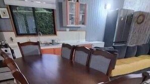 Una mesa de comedor con seis sillas, una zona de cocina con refrigerador y piso de baldosas.
