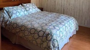 Un dormitorio con techo de madera, una cama con ropa de cama estampada y cuadros colgados en la pared.
