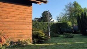 Un edificio de madera con techo inclinado, rodeado de un césped cuidado y varios arbustos.