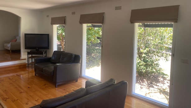 A spacious living room with a flat-screen TV, a grey sofa, and a wooden floor. - Country cottage in the heart of the Yarra Valley (Seville)