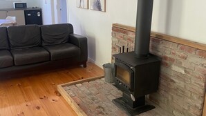 A living room with a black wood-burning stove, a black sofa, wooden flooring, and a brick accent wall. - Country cottage in the heart of the Yarra Valley (Seville)