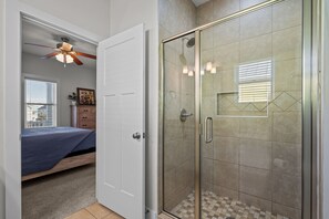 Ein Schlafzimmer mit einem Bett, einem Deckenventilator und einer Tür zu einem Duschbereich mit Glastüren und gefliesten Wänden.