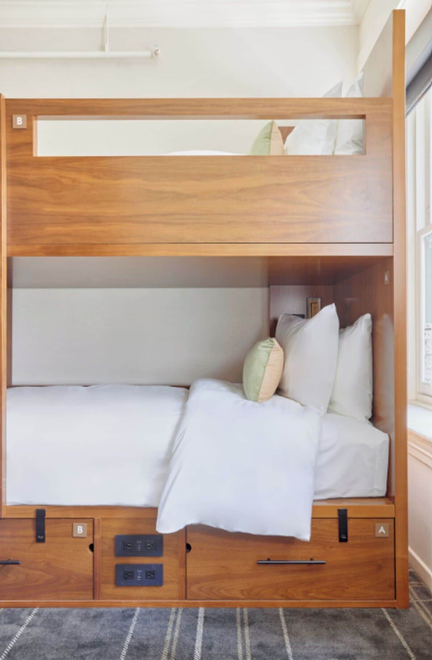 Una cama litera con estructura de madera, ropa de cama blanca y un pequeño cajón con cerradura.