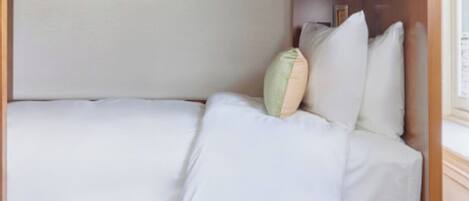 Una cama litera con estructura de madera, ropa de cama blanca y un pequeño cajón con cerradura.