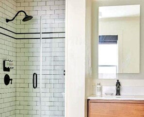 A bathroom with white tiled walls, a wooden vanity, a mirror, and a shower with a black faucet. - Bposhtels San Francisco (San Francisco)