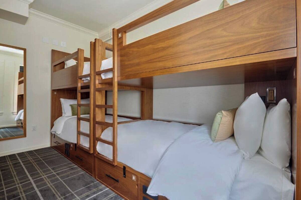 A bunk bed room with a wooden ladder, white bedding, and a plaid carpet.