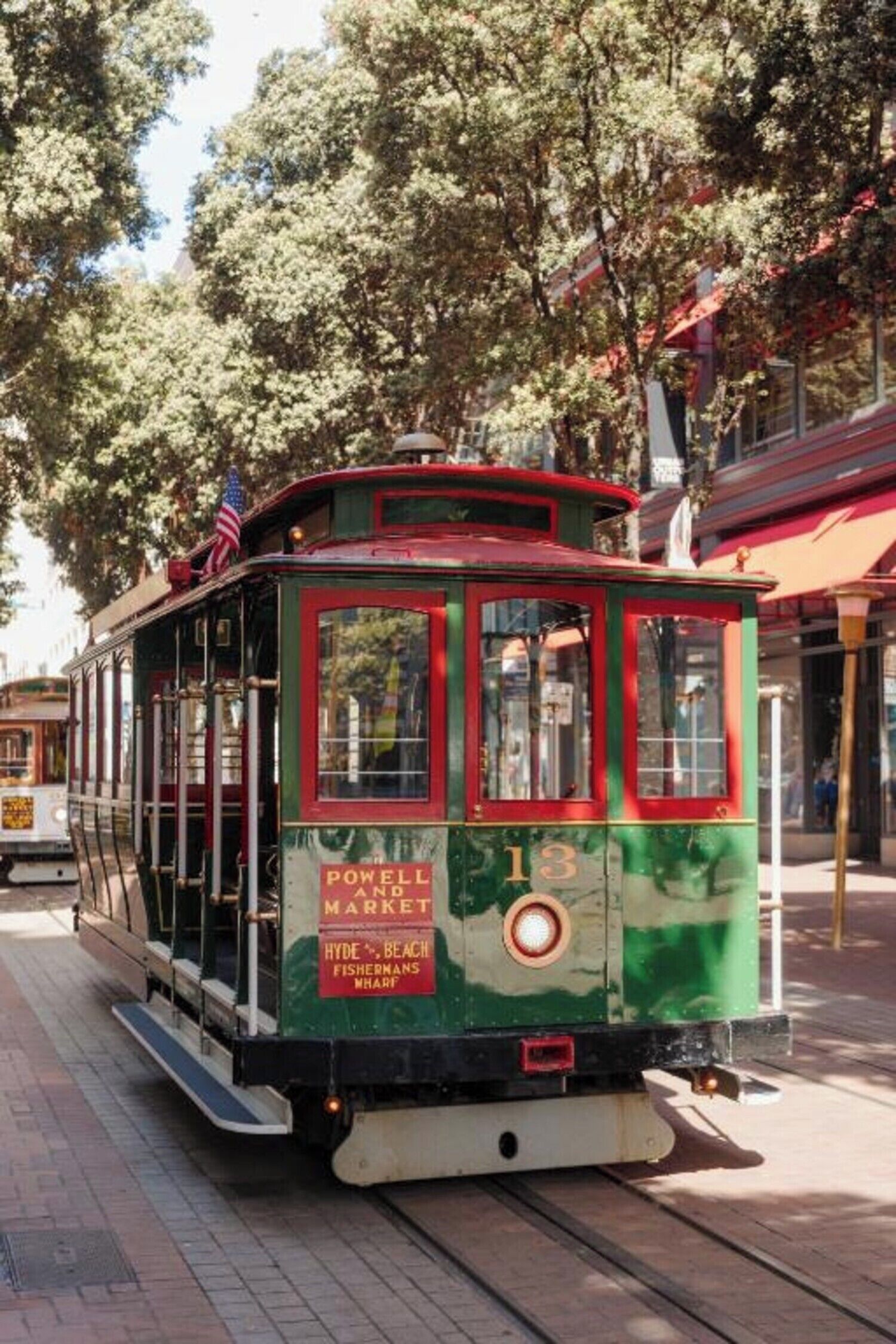 A green trolley with red trim and a sign reading "Powell and Market Hyde Beach Fisherman's Wharf."