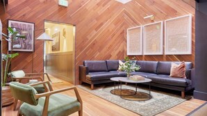 A modern living room with a herringbone wood floor, a dark leather sofa, a round coffee table, and a green armchair.