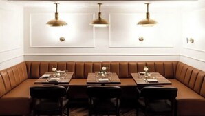 A restaurant with a brown booth seating area, wooden tables, and black chairs.