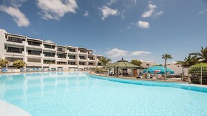 Une piscine avec des chaises longues, un belvédère et un bâtiment doté de plusieurs balcons.