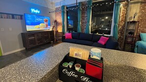 Un soggiorno moderno con angolo bar, una TV che mostra una pubblicità e vista sulla città di notte.