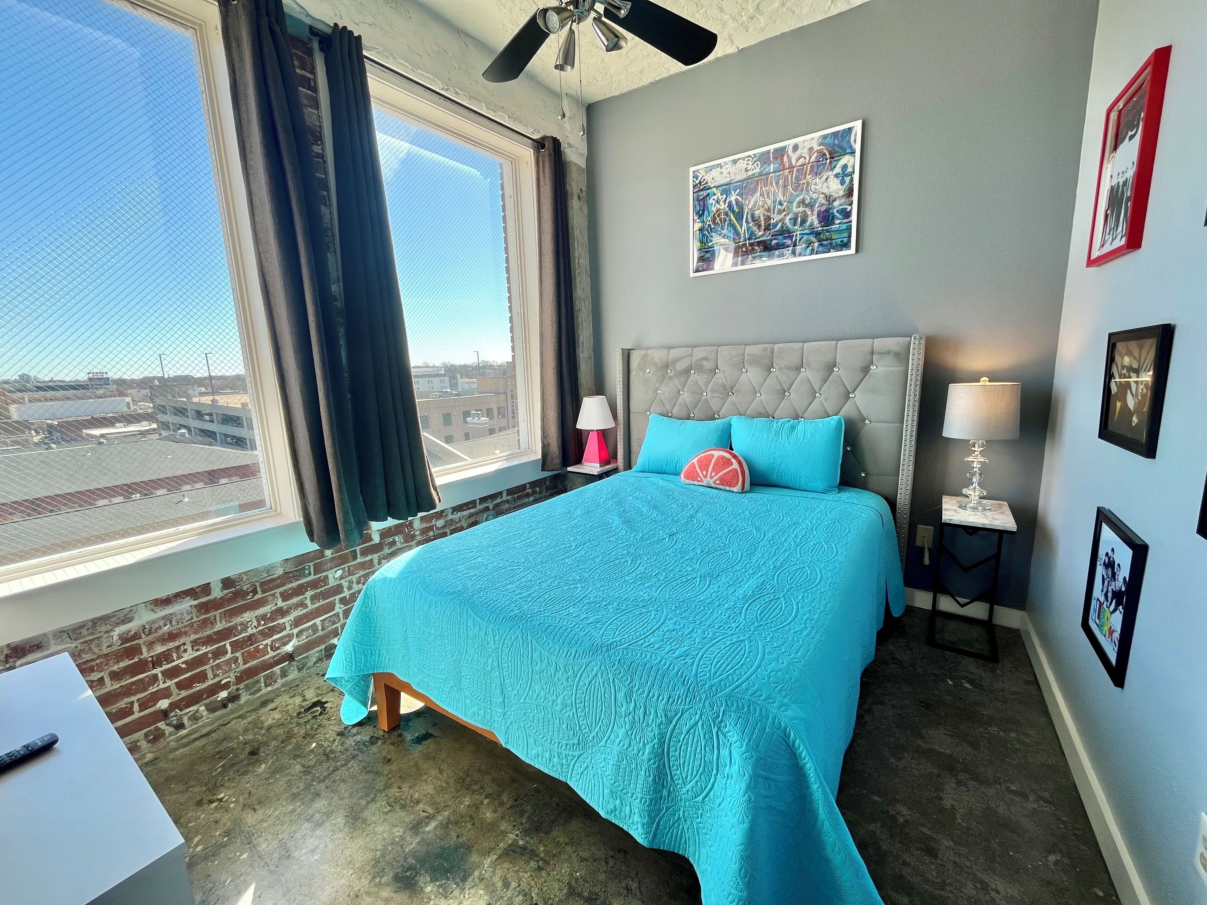 A bedroom with a large bed, a window with curtains, a ceiling fan, and a city view.