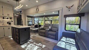 A modern RV interior with a kitchen, dining area, and seating space. - S'mores & Stars: The Ultimate Family RV Rental 235 (River Ranch)