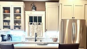 A kitchen with two dark wooden bar stools, a stainless steel refrigerator, and a window with a curtain.