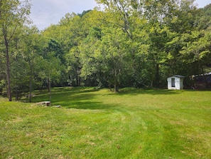 A grassy field with a small white building, surrounded by dense trees.