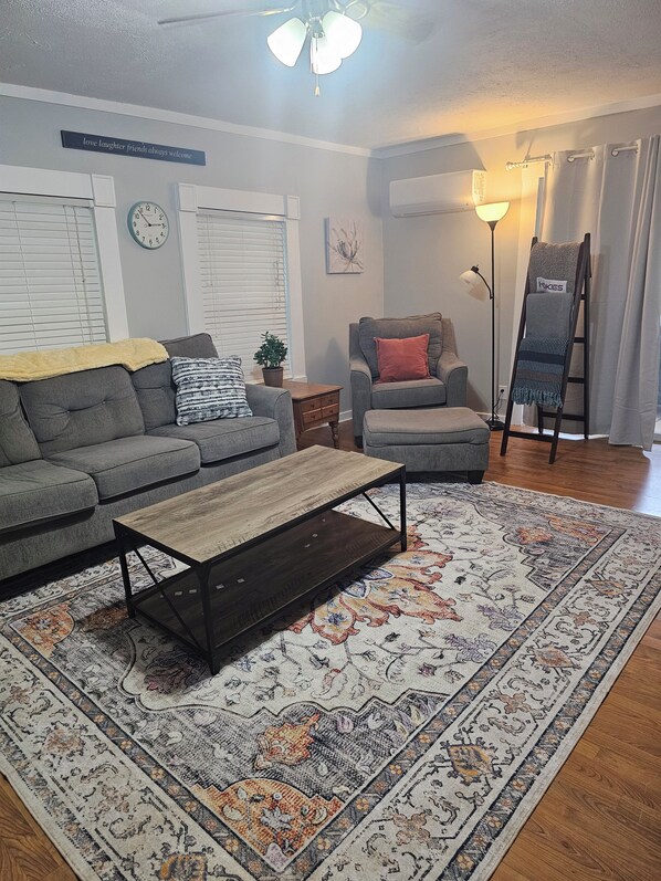 A living room with a sofa, armchair, coffee table, and a patterned rug.