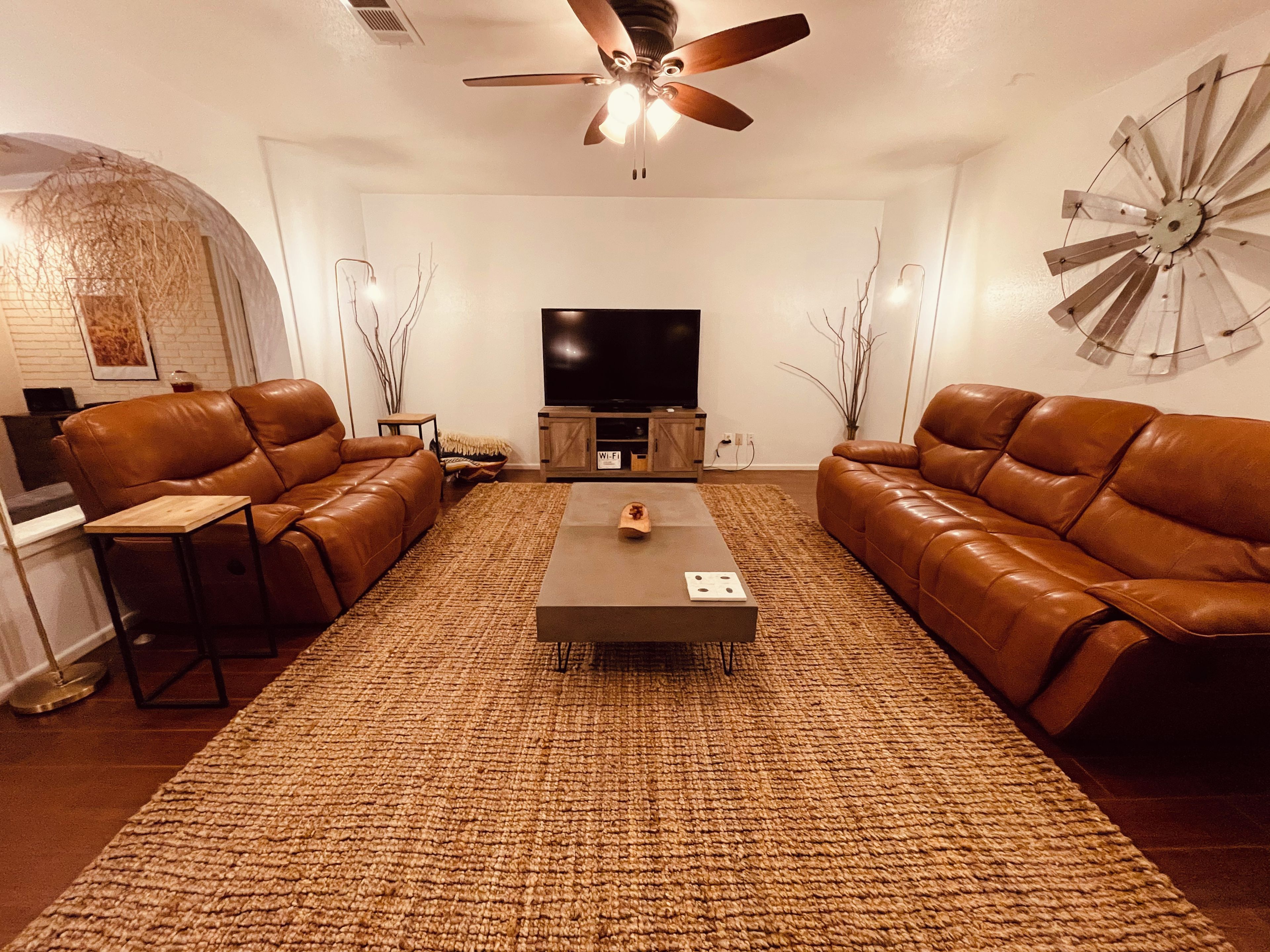 Ein Wohnzimmer mit braunem Ledersofa, einem Couchtisch, einem Fernseher und einer Wanddekoration.