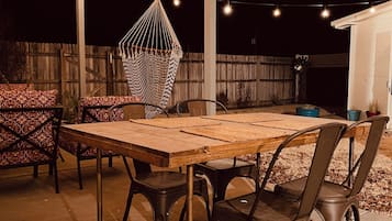 Eine Terrasse im Freien mit einem Holztisch, Metallstühlen, einer Hängematte und Lichterketten.