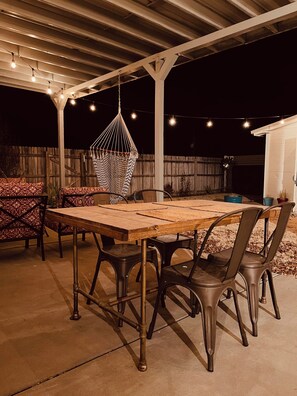 Eine Terrasse im Freien mit einem Holztisch, Metallstühlen, einer Hängematte und Lichterketten.