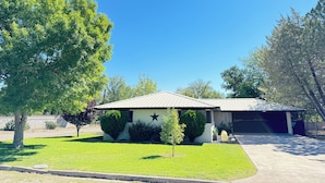 Uma casa residencial com garagem, gramado bem cuidado e uma árvore grande.