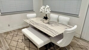 Un área de comedor con una mesa de mármol, sillas blancas acolchadas, un banco y una alfombra estampada.
