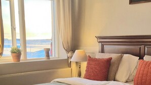 Un letto rifatto con cura, una coperta a motivi, una lampada da comodino e vista sull'esterno attraverso una finestra con tende.