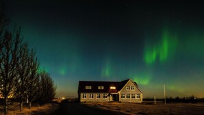 Una casa dal tetto scuro e dalle pareti bianche, immersa in un paesaggio innevato sotto un cielo notturno stellato.