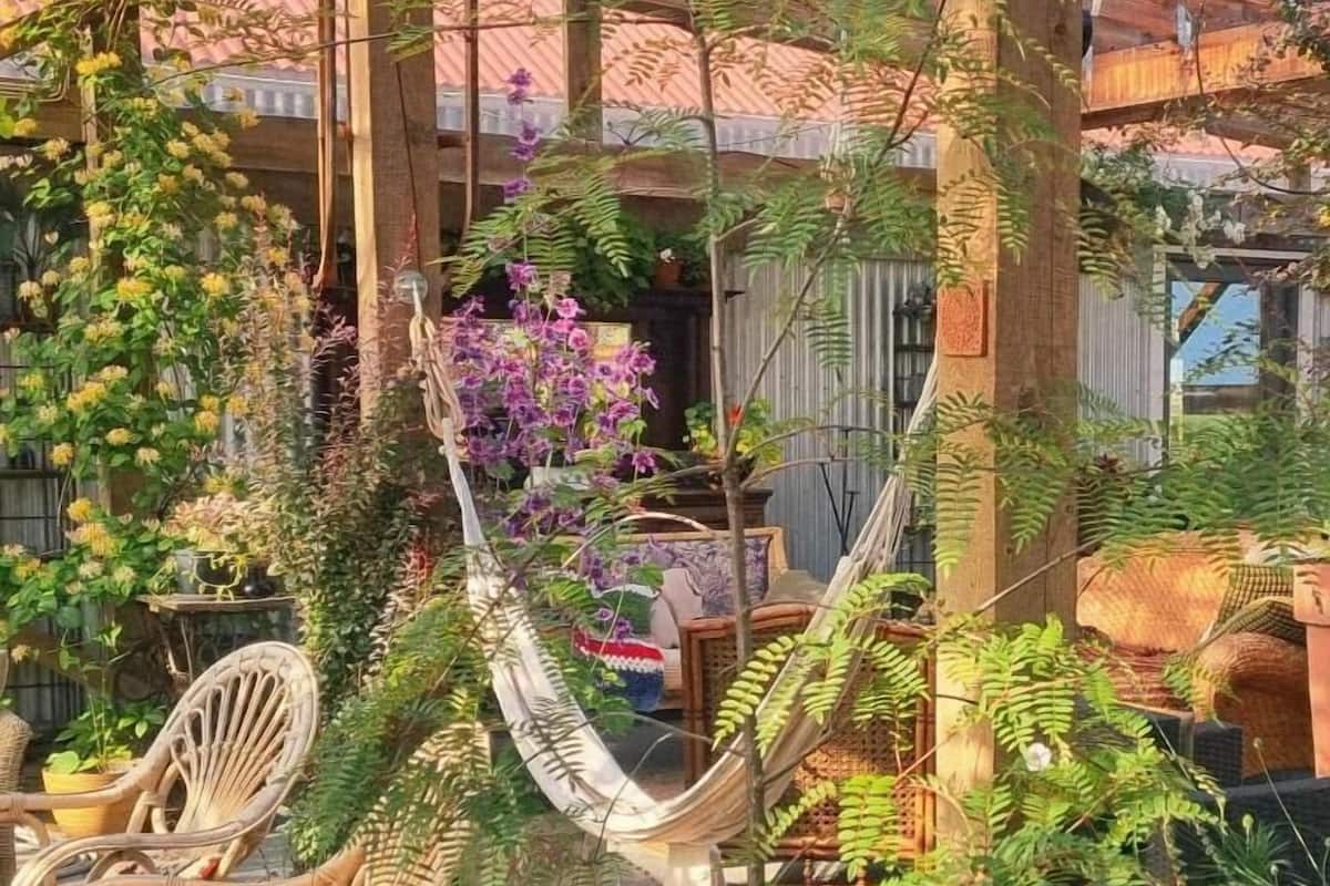 A hammock in a garden area with chairs and potted plants.