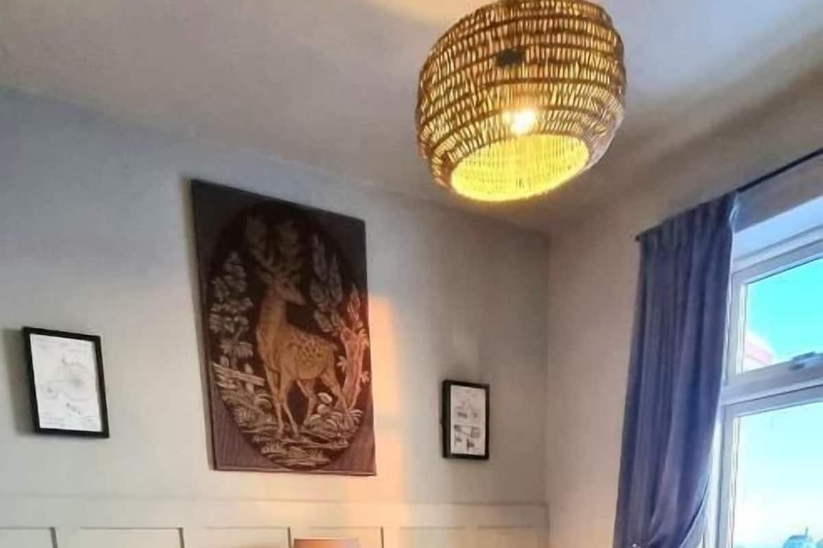 A hotel room with two beds, a chandelier, a window with curtains, and framed artwork on the wall.