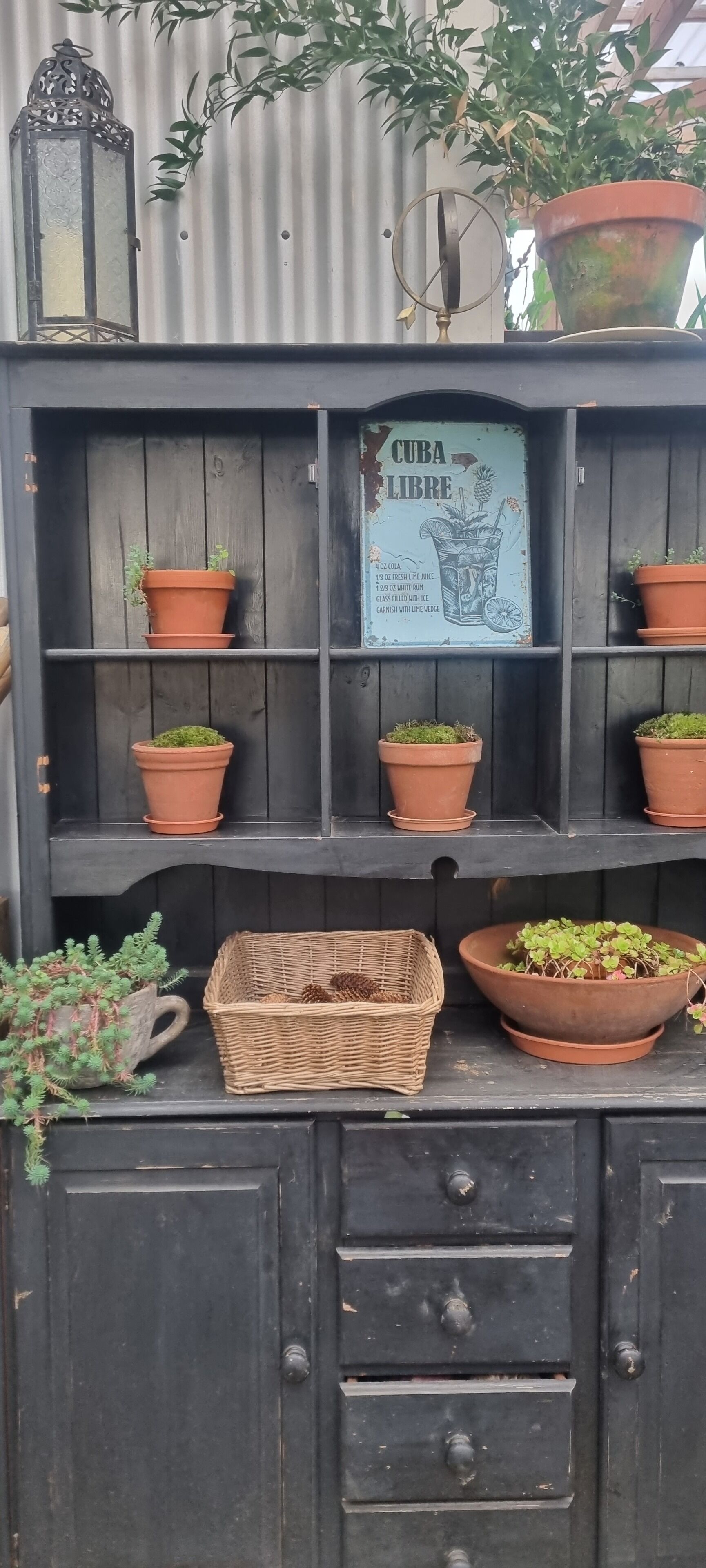 Una estantería de madera con macetas de terracota y una cesta de mimbre.