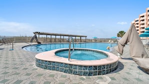 Een zwembad met een jacuzzi, ligbedden en een houten terras.