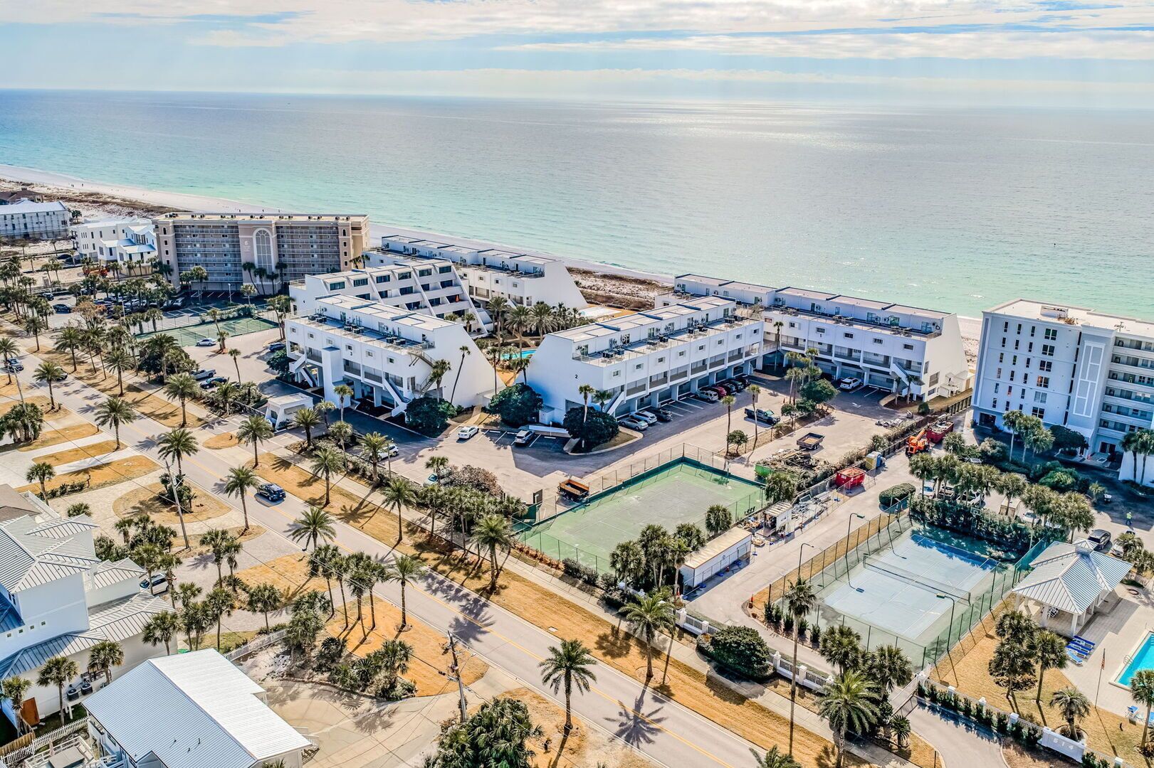 Eine Luftaufnahme eines Hotelkomplexes an der Küste, mit mehreren Gebäuden, einem Strand und Palmen.