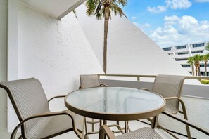 A round glass table with wicker chairs on a balcony with white walls and a palm tree. - Aegean 209 near beach overlooks pool! (Destin)