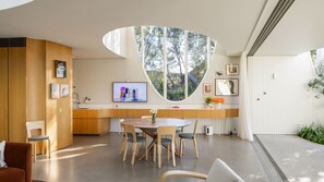 A modern kitchen with a curved window, wooden cabinetry, and a dining area with a round table and chairs. - Curva, Glebe - Hosted by L'Abode (Glebe)