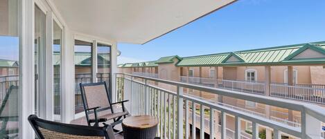 A balcony with wicker chairs and a small round table, overlooking a building with green roofs.