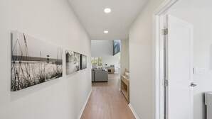 A hallway with wooden flooring, white walls, and a door leading to a room. - Salt + Sol | Heated Pool |Canal-Front | Golf Cart | Dock (Anna Maria)