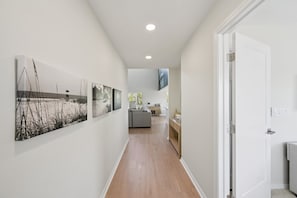 A hallway with wooden flooring, white walls, and a door leading to a room. - Salt + Sol | Heated Pool |Canal-Front | Golf Cart | Dock (Anna Maria)