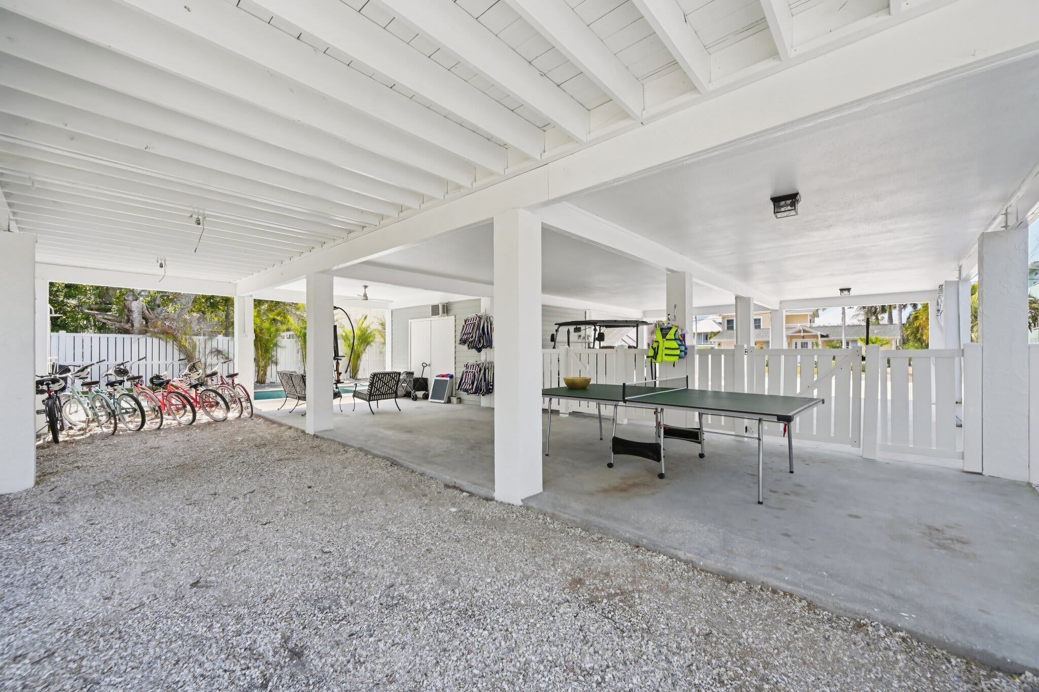 A covered outdoor area with a ping pong table, bicycles, and a white fence.