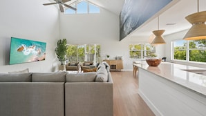 A spacious living area with a large sofa, a dining table, and a kitchen counter. - Salt + Sol | Heated Pool |Canal-Front | Golf Cart | Dock (Anna Maria)
