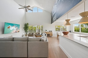A spacious living area with a large sofa, a dining table, and a kitchen counter. - Salt + Sol | Heated Pool |Canal-Front | Golf Cart | Dock (Anna Maria)