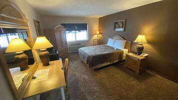 A hotel room with a bed, bedside lamps, a desk with a chair, a dresser, and a window with blinds.