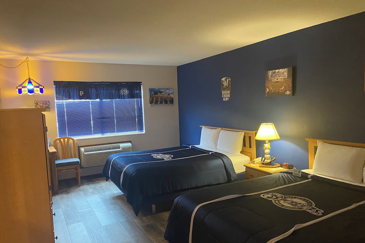 Habitación de hotel con dos camas, un escritorio, una silla, una ventana con persianas, un calentador y adornos en la pared.