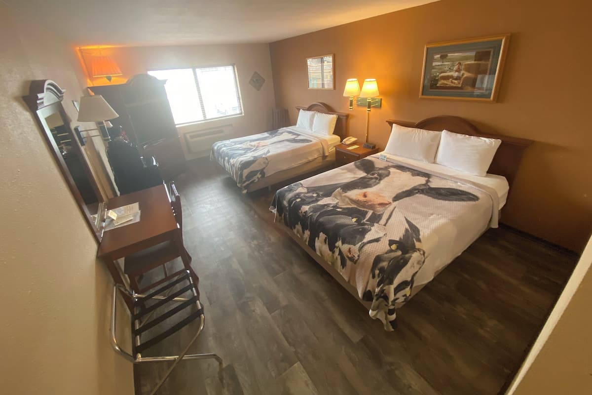 Habitación de hotel con dos camas, un escritorio, una silla, una lámpara y un cuadro en la pared.