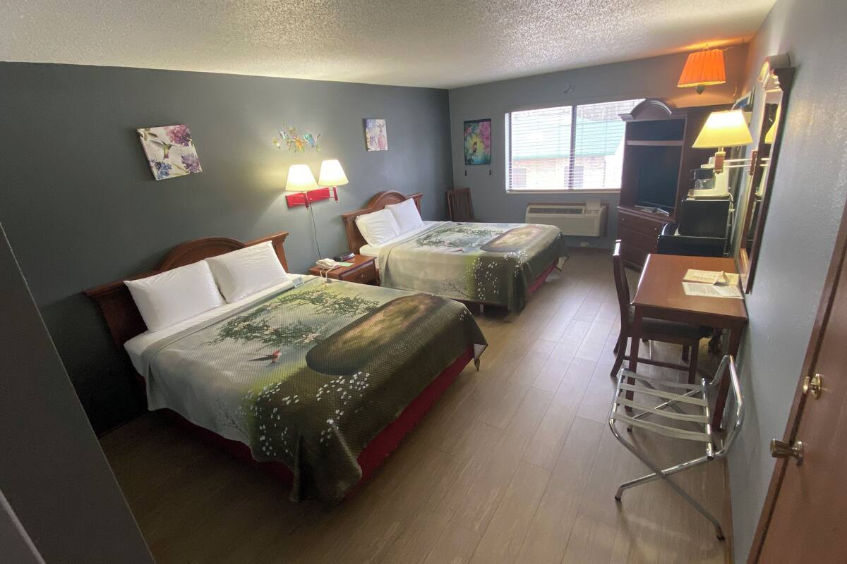 Habitación de hotel con dos camas, un escritorio, una silla y una ventana con persianas.