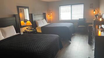 Ein Hotelzimmer mit zwei Betten, einem Schreibtisch, einem Stuhl, einer Lampe und einem Fenster mit Jalousien.