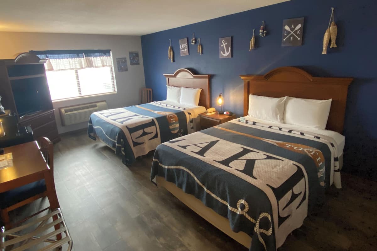 Habitación de hotel con dos camas, un escritorio, una silla, un televisor y una ventana con persianas.