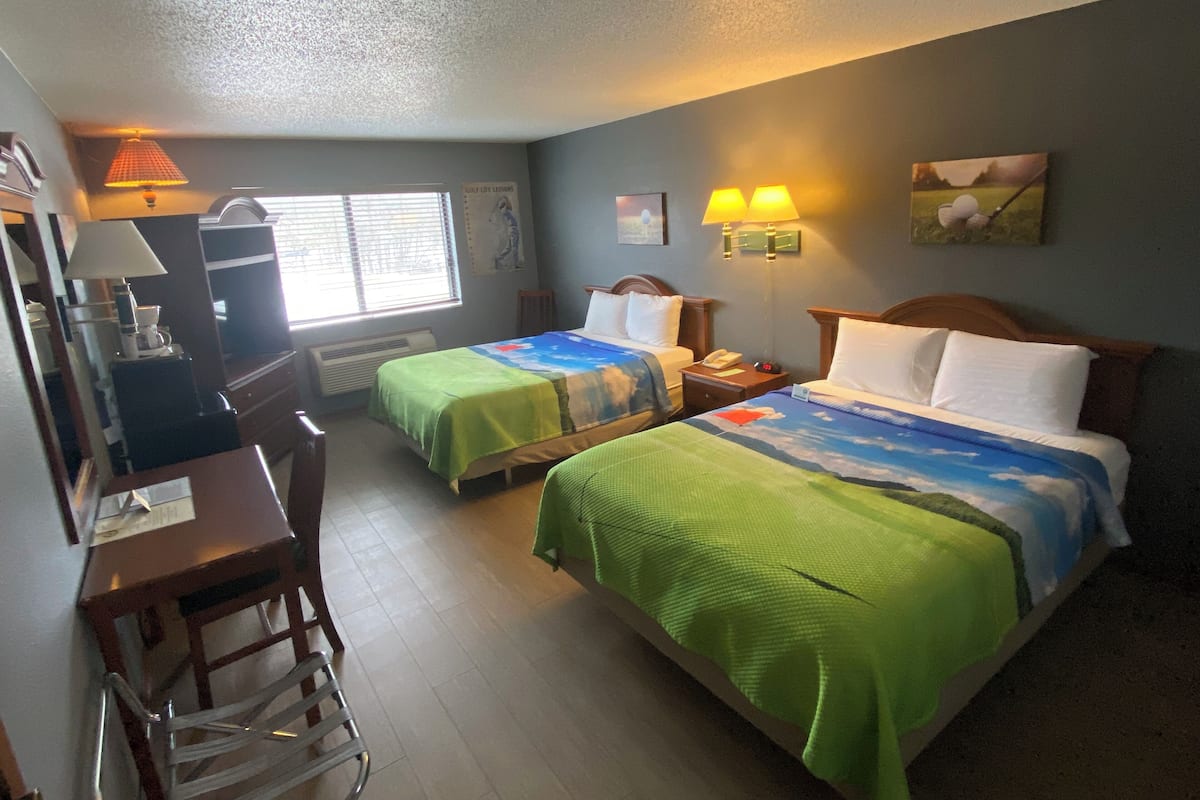 Una habitación de hotel con dos camas, un escritorio, una silla, una lámpara y un cuadro en la pared.