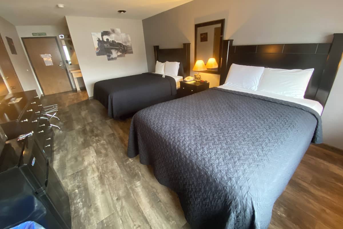 Habitación de hotel con dos camas, un escritorio y una silla. Hay un televisor montado en la pared y una puerta que da a otra habitación.