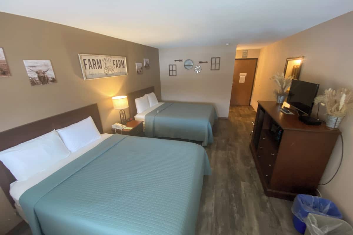 Habitación de hotel con dos camas, un escritorio con ordenador, televisor y espejo.